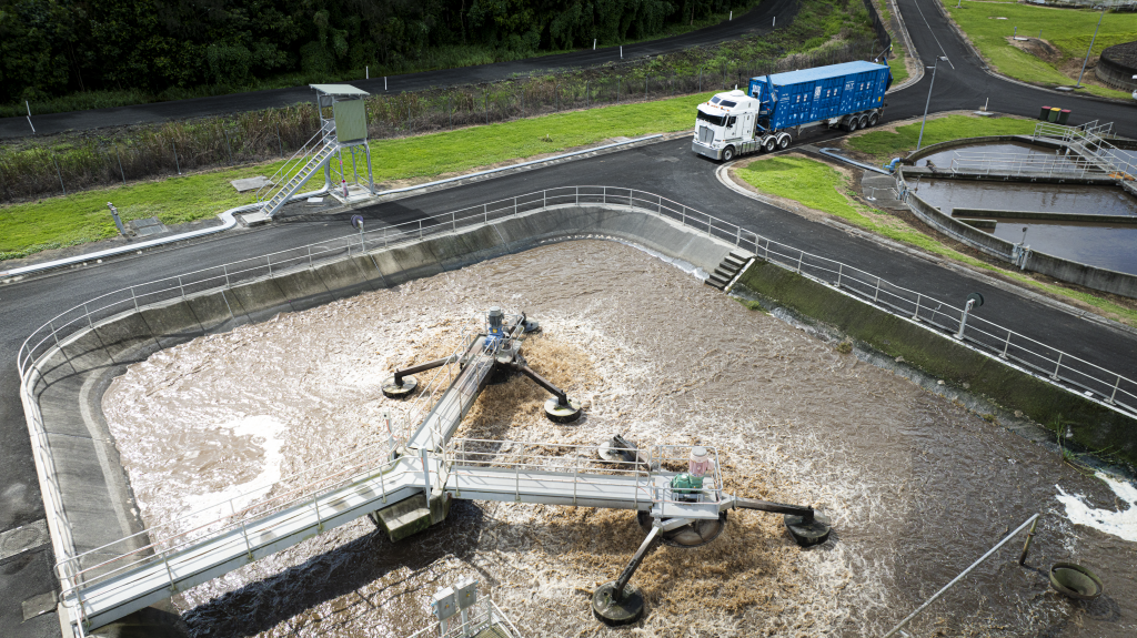 Aerial view of a wastewater treatment plant's aeration basin with a three-armed mechanical mixer, surrounding walkways, and a blue truck nearby.
