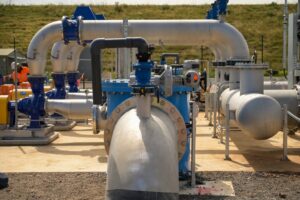 Industrial piping system with large stainless steel pipes, blue valves, and a pump at an outdoor facility