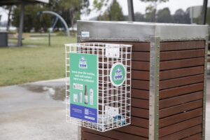 A-Return-and-Earn-bin-basket-in-Batemans-Bay-1024x683 | Empower Stories | Build Authority - Drive Impact White metal wire recycling cage attached to a wooden park bin with a green sign about returning bottles and cans for 10¢.
